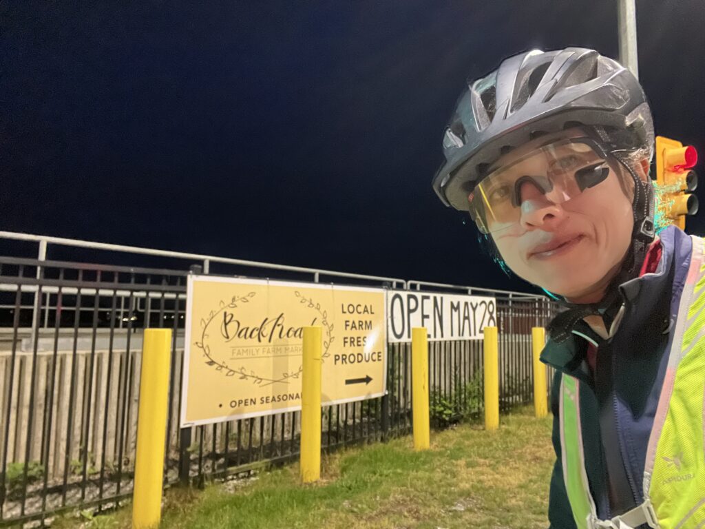 Dara posing in front of Back Road Family Farm Produce sign in Delta